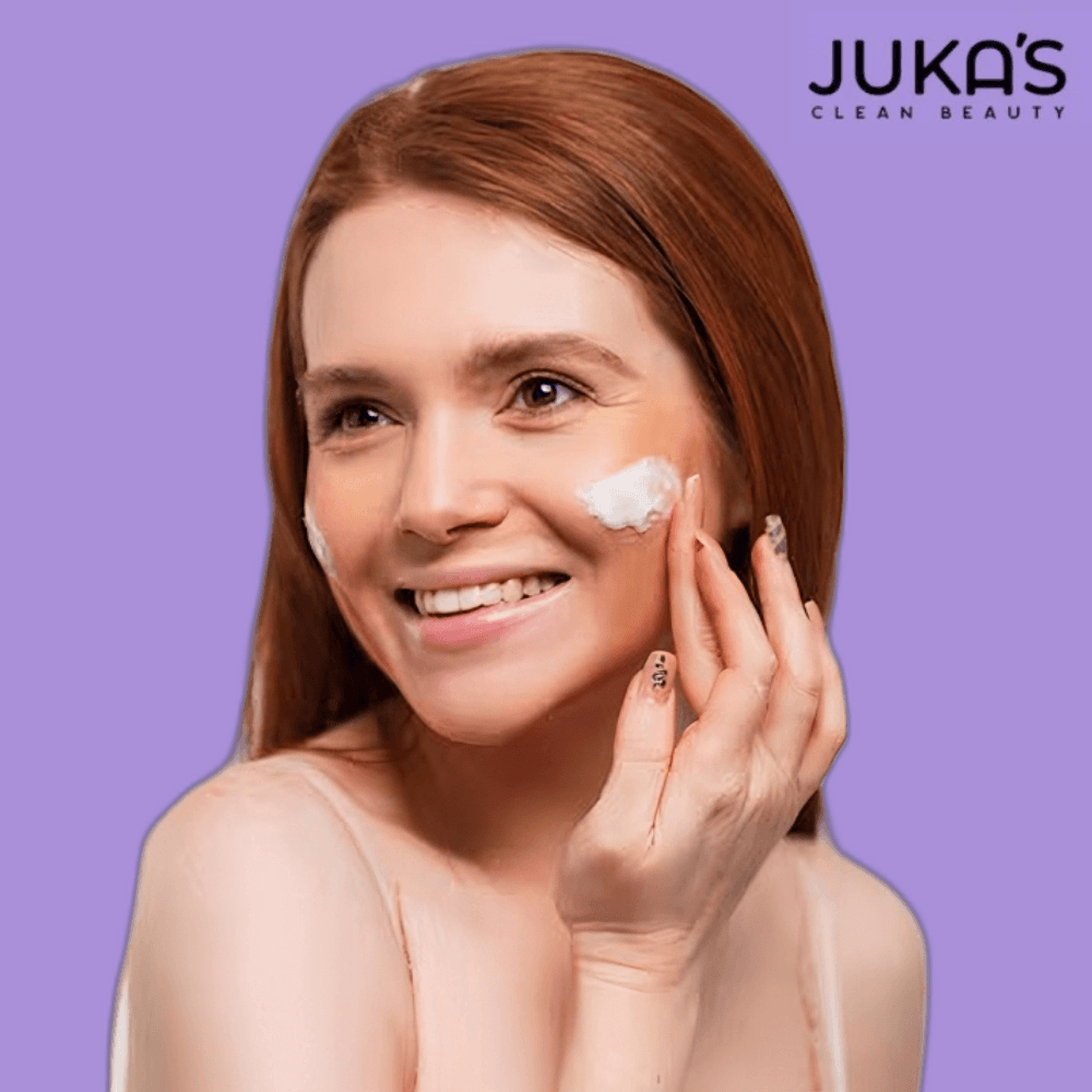Woman applying cream from Juka's Skincare Set for Combination Skin on her face, smiling against a purple background.
