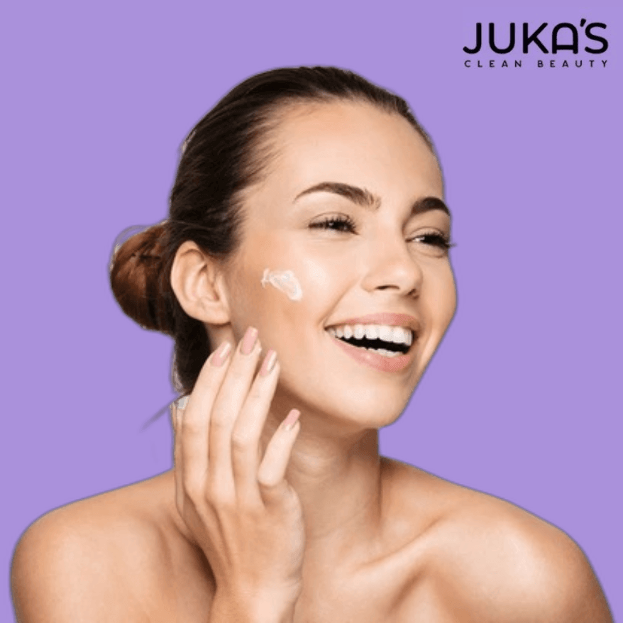 A woman applying Juka's Clean Beauty Natural Skin Cleansers on her face, showcasing a radiant smile and healthy skin.