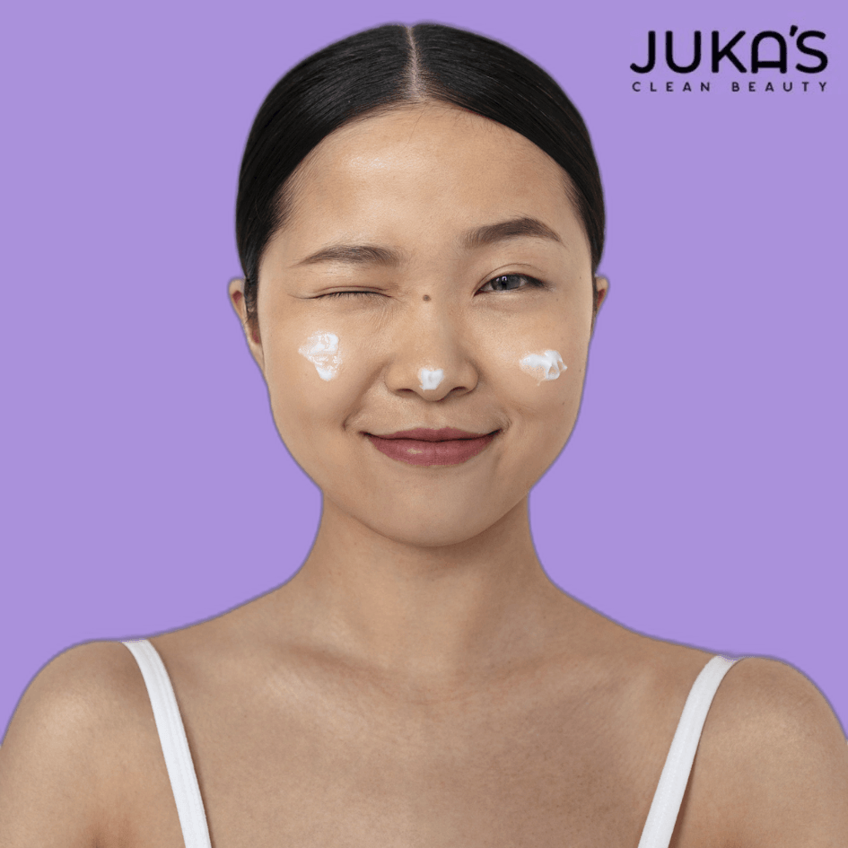 Woman applying Juka's natural face moisturizer for radiant skin on a purple background.